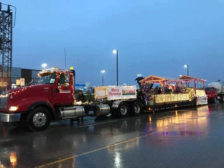 Photo of Gwillimdale Farms' float at the Bradford Christmas Parade 2017. A red truck cab is pulling a long trailer covered carrying two gazebos trimmed with Christmas lights. A box on the rear wheels of the cab, in front of the trailer has a banner lined in Christmas lights, which reads "Merry Christmas", to the left of the Gwillimdale Farms logo.