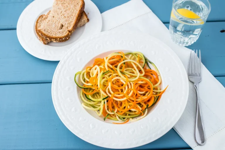 A bowl of spiralized orange, green, and yellow vegetables, speckled with black pepper.