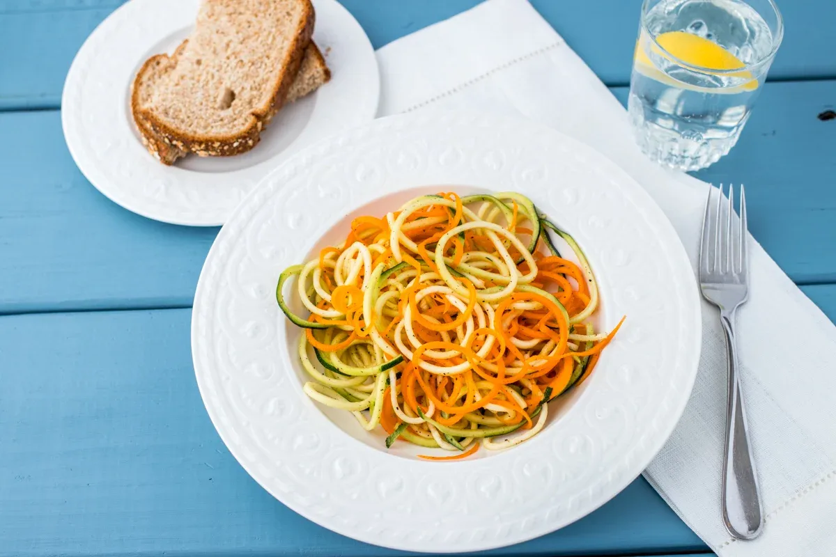 A bowl of spiralized orange, green, and yellow vegetables, speckled with black pepper.