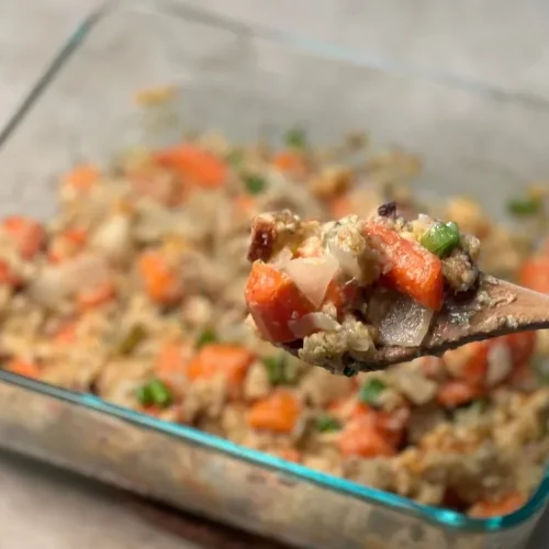 A glass casserole dish of Carrot Casserole. A wooden spoon holds a scoop of the casserole closer to the camera.