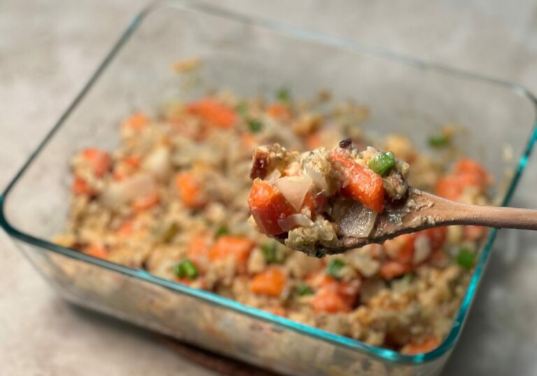 A glass casserole dish of Carrot Casserole. A wooden spoon holds a scoop of the casserole closer to the camera.