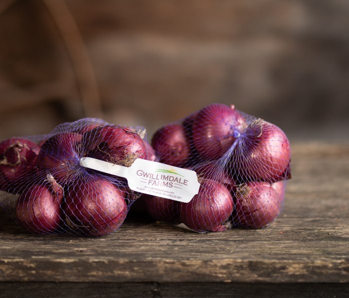 Two bags of Gwillimdale Farms red onions resting on an unfinished wooden table.
