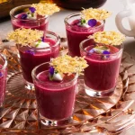 Five shot glasses filled with a thick, vibrant fuschia-coloured liquid, and topped with violet pedals, micro-greens, and a parmesan crisp.