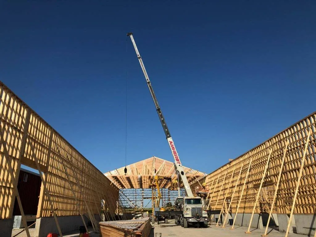 Construction of one of our new sustainable storage facilities: the view from inside a long wood-framed structure. The wall at the end has the pointed shape of a gabled roof, yet to be installed. Above the newly constructed walls, a clear deep blue sky is visible. There is a truck with a tall crane parked inside the structure, with its crane raised high up above the height of the walls around it.
