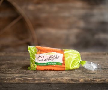 A 2lb bag of Gwillimdale Farms carrots, sitting on a rustic wooden table.