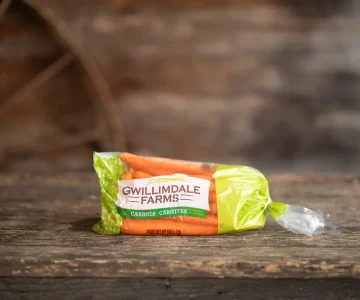 A 2lb bag of Gwillimdale Farms carrots, sitting on a rustic wooden table.