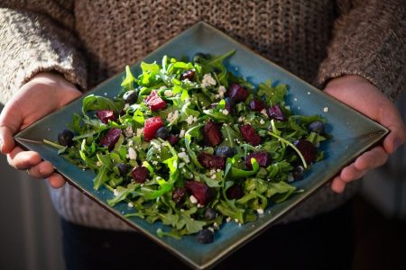 A raw beet salad, with arugula, and berries, served on a square dish.