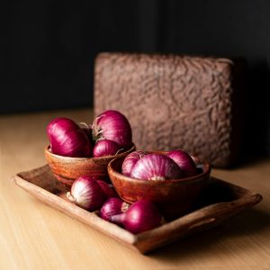 Red onions in a dimly lit room, sitting in wooden bowls in the center of a table.