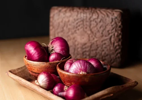 Red onions in a dimly lit room, sitting in wooden bowls in the center of a table.
